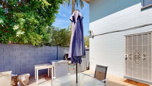 Eine Terrasse im Freien mit einem Glastisch, Stühlen und einem violetten Sonnenschirm.