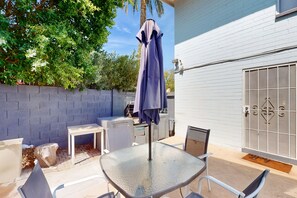 An outdoor patio with a glass table, chairs, and a purple umbrella. - Snowbird-Friendly Condo with Patio Access, Central AC, Free WiFi - Dogs Welcome (Glendale)