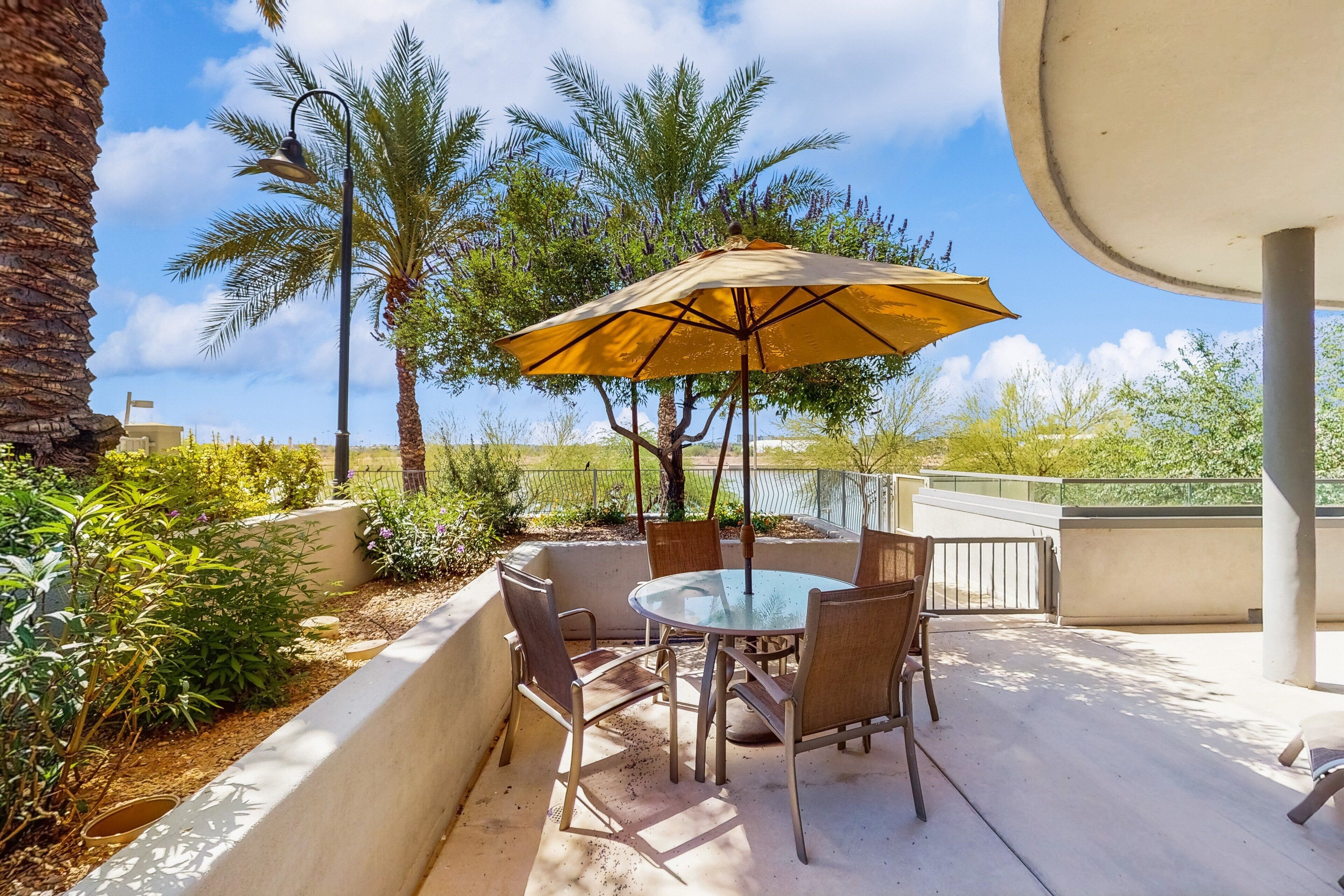 Une terrasse extérieure avec une table ronde en verre, quatre chaises et un seul parasol jaune.