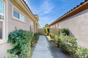 A narrow concrete pathway flanked by buildings with beige stucco walls and red-tiled roofs. - Mountain view home, private pool & spa - shared pools, tennis, fitness center (Cathedral City)