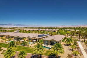 A resort with multiple villas, each featuring a swimming pool, surrounded by palm trees and a clear view of distant mountains. - Mountain view home, private pool & spa - shared pools, tennis, fitness center (Cathedral City)