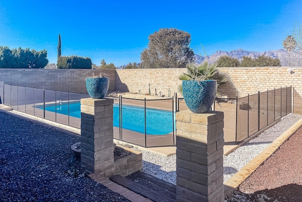 Une piscine offrant une vue dégagée sur les montagnes en arrière-plan, entourée d’un mur de briques et d’une clôture en métal.