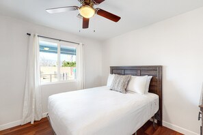 A bedroom with a bed, a ceiling fan, a window with curtains, and a view of greenery outside.