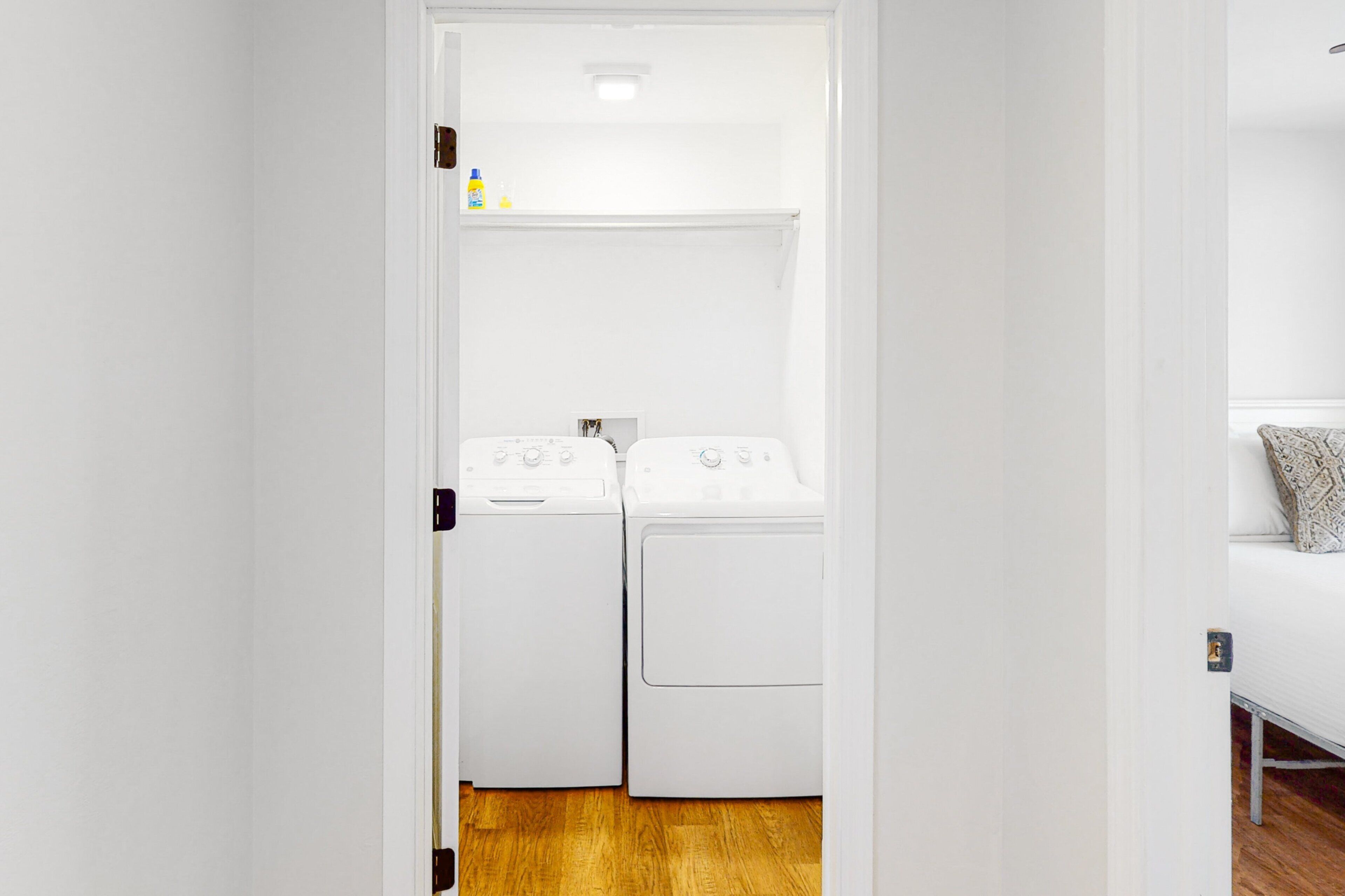 A laundry room with two white washing machines, a wooden floor, and a white door.