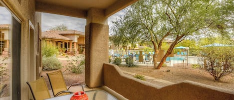 A covered patio with a table and chairs, a ceiling fan, and a view of a swimming pool and trees.