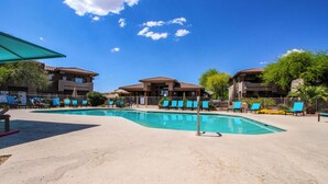 A swimming pool area with lounge chairs and a building with a tiled roof. - Comfortable condo with renovated kitchen, patio, pool, hot tub & fitness center (Oro Valley)