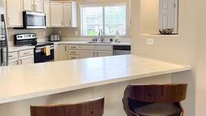 A kitchen with white cabinets, a large island, and two wooden chairs. - Comfortable condo with renovated kitchen, patio, pool, hot tub & fitness center (Oro Valley)