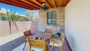 An outdoor patio with a wooden table and chairs, a brick wall, and a window with green shutters. - Stylish Sam Hughes Escape With Private Yard, Dogs OK & Free WiFi (Tucson)