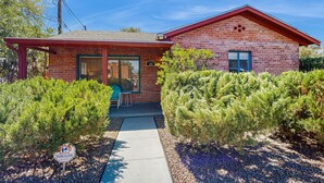 A single-story brick house with a red roof, a visible number '123' on the front, and a covered porch with a chair. - Stylish Sam Hughes Escape With Private Yard, Dogs OK & Free WiFi (Tucson)