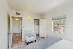 A bedroom with a bed, a chair, a wardrobe, a window, and a door leading to another room. - Stylish Sam Hughes Escape With Private Yard, Dogs OK & Free WiFi (Tucson)