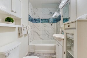 A bathroom with a toilet, sink, and bathtub. There is a shelf with a plant and towels. The walls have a marble pattern and a blue-tiled shower area. - Stylish Sam Hughes Escape With Private Yard, Dogs OK & Free WiFi (Tucson)