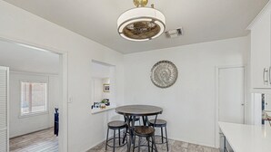A modern kitchen with a round dining table and four stools, a decorative wall piece, and a ceiling light fixture. - Stylish Sam Hughes Escape With Private Yard, Dogs OK & Free WiFi (Tucson)