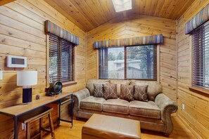 Ein gemütliches Blockhauss-Interieur mit Holzausstattung, einer Couch, einem Tisch mit Lampe und einem Ventilator.
