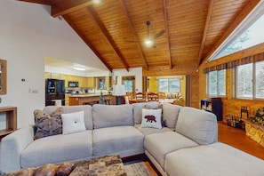 A spacious living area with a large sectional sofa, wooden ceiling beams, and a view of the kitchen and dining area. - Cozy Home w/ private hot tub, deck, office space, & board games - dog-friendly (Munds Park)