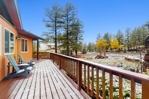 Eine Holzterrasse mit Adirondack-Stühlen, einem Hollergeländer und Blick auf Bäume und einen Garten.