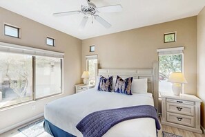 A bedroom with a bed, nightstands, a ceiling fan, and windows. - Renovated condo with updated floors, pool, hot tub & mountain views (Oro Valley)