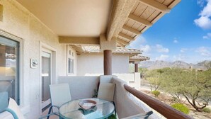 Een balkon met een glazen tafel en stoelen, een uitzicht op het woestijnlandschap en een gebouw met een stukwerk gevel.