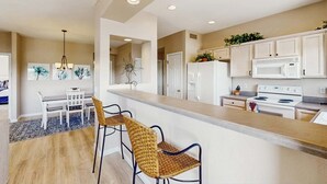 Een moderne keuken met witte kasten, een centraal eiland en een eethoek met een tafel en stoelen.