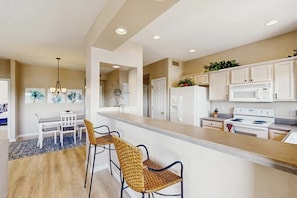 A modern kitchen with white cabinets, a central island, and a dining area with a table and chairs. - Renovated condo with updated floors, pool, hot tub & mountain views (Oro Valley)