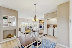 A modern kitchen with white appliances, a dining area with a wooden table and chairs, and a living room with a sofa and a TV. - Renovated condo with updated floors, pool, hot tub & mountain views (Oro Valley)