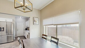 A spacious dining area with a large table and chairs, a kitchen with stainless steel appliances, and a large window with blinds.