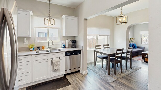 A modern kitchen with stainless steel appliances, white cabinetry, and a dining area with a wooden table and chairs.