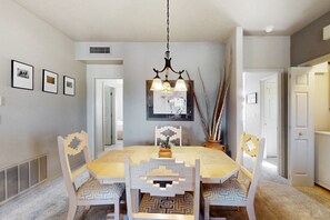 A dining area with a round table, four chairs, a chandelier, and framed pictures on the wall. - Comfy, dog-friendly condo with mountain views, pool, hot tub & gym (Oro Valley)