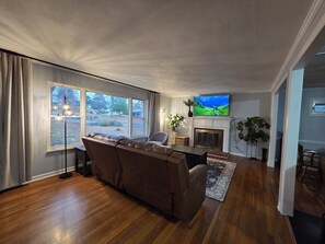 A living room with a fireplace, a large TV, and a sofa. - Great location: UT, Windorck, national lab, melton lake park (Oak Ridge)