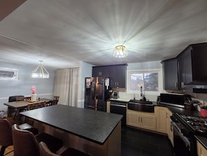 A modern kitchen with dark cabinets, a central island, a dining area with a table and chairs, and a window with a view of trees. - Great location: UT, Windorck, national lab, melton lake park (Oak Ridge)