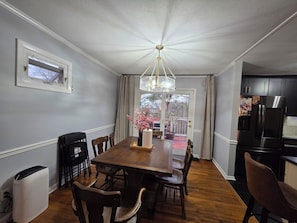A dining area with a wooden table, chairs, a chandelier, and a view through a glass door to an outdoor deck. - Great location: UT, Windorck, national lab, melton lake park (Oak Ridge)