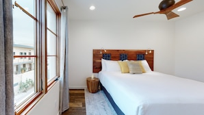 Un dormitorio con una cama grande, cabecera de madera, ventilador de techo y vista por una ventana.