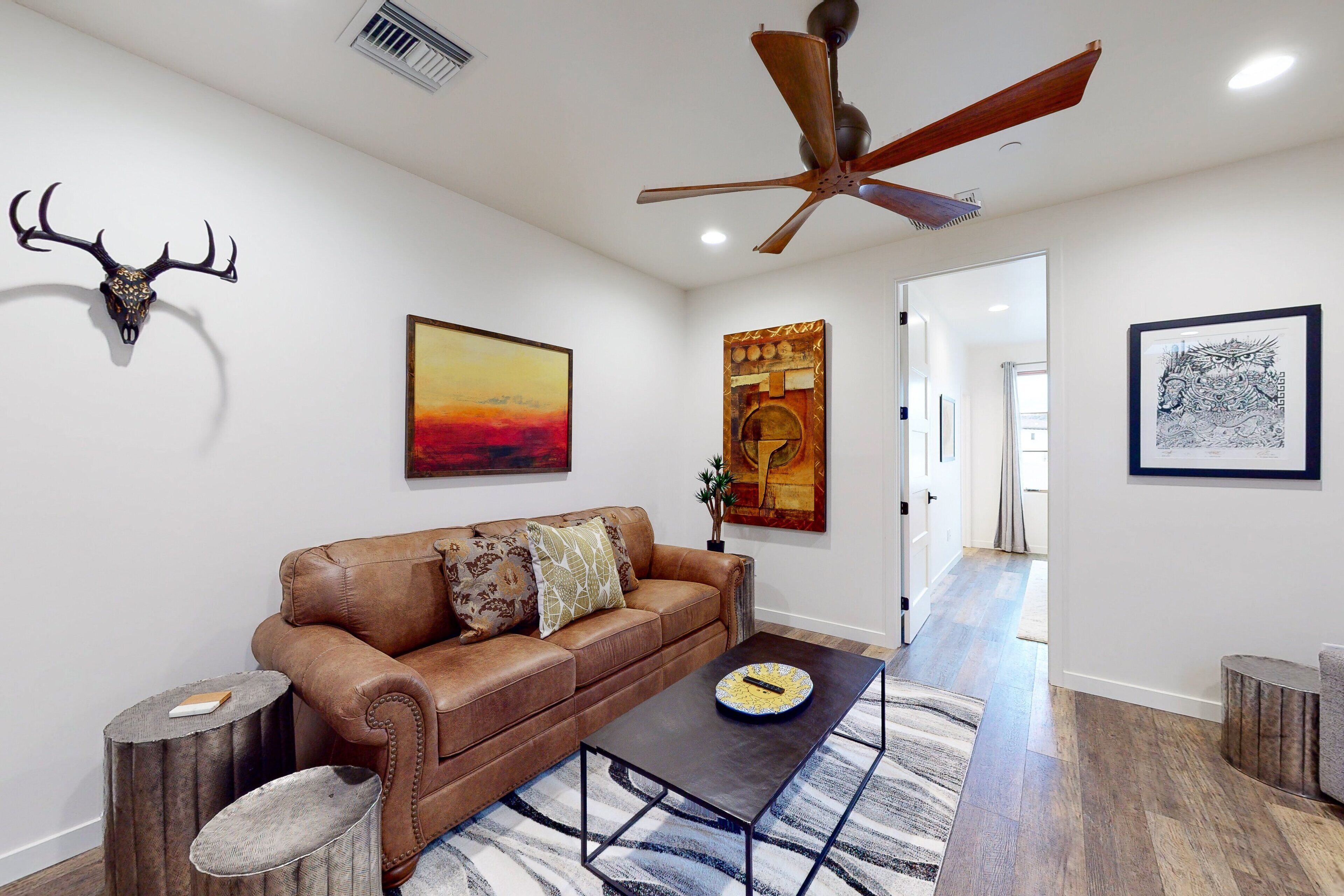 A living room with a brown leather sofa, a coffee table, a ceiling fan, and a mounted deer skull.