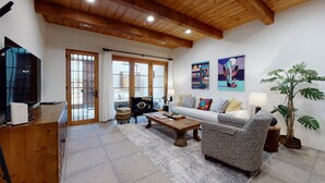 Un salón amplio con techo de madera, un sofá, un sillón estampado, una mesa de centro y un televisor.