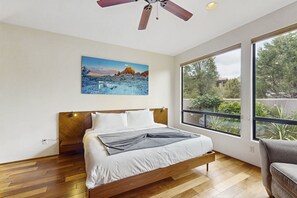 Een slaapkamer met een bed, een raam, een plafondventilator en een schilderij aan de muur.