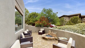 Une terrasse extérieure aménagée avec des meubles en osier, un foyer et une vue sur la verdure environnante.