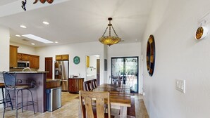 Une cuisine spacieuse avec des meubles de rangement en bois, un coin repas doté d’une grande table et de chaises en bois, et un lustre moderne.