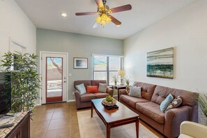 A living room with a ceiling fan, two sofas, a coffee table, a TV, and a door leading outside. - Beautifully remodeled dog-friendly Casita with shared heated pool & hot tub (Tucson)