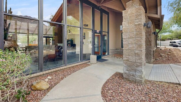 A modern building with large glass windows, a stone pillar, and a covered entrance. - Snowbird-friendly condo w/shared heated outdoor pool, hot tub & tennis (Tucson)