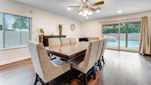 A dining room with a wooden table and six chairs, a ceiling fan, and a view of a swimming pool through glass doors. - Dog-friendly home with enclosed yard, pool, putting green, grill, foosball, & AC (Scottsdale)