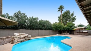 A swimming pool with a stone wall and a palm tree in the background. - Dog-friendly home with enclosed yard, pool, putting green, grill, foosball, & AC (Scottsdale)