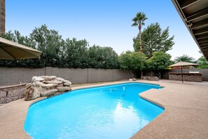 A swimming pool with a stone wall and a palm tree in the background. - Dog-friendly home with enclosed yard, pool, putting green, grill, foosball, & AC (Scottsdale)