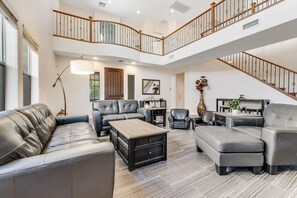 A spacious living room with a high ceiling, a staircase, and a view of the outdoors.