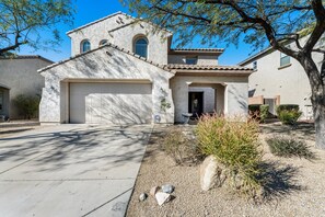 A two-story house with a garage, a front door, and a small garden with a rock and shrubs.
