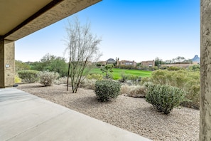 A patio area with a view of a landscaped garden and distant buildings. - Golf-Course View Condo with Central AC & Washer/Dryer - Shared Pool & Hot Tub (Scottsdale)