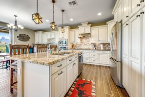 A spacious kitchen with white cabinetry, granite countertops, and a large island. There are pendant lights, a built-in oven, and a refrigerator. - Golf-Course View Condo with Central AC & Washer/Dryer - Shared Pool & Hot Tub (Scottsdale)