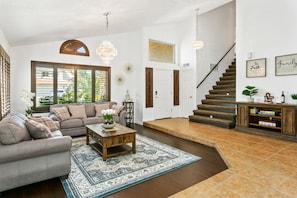 Un salon spacieux avec un grand canapé, une table basse et un tapis. Un escalier mène à l’étage supérieur.