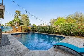 Une piscine dotée d’une terrasse carrelée, entourée d’une végétation luxuriante et illuminée par une guirlande lumineuse.