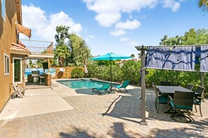 Un jardin avec une piscine, des chaises longues, un espace barbecue et une terrasse couverte.