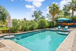 A swimming pool with a tiled edge, surrounded by palm trees and a lounge area with chairs and an umbrella. - Dog-Friendly Gem near Golf Course W/ Private Pool, Fast WiFi & Central AC (Avondale)