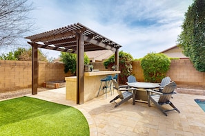 Une terrasse extérieure dotée d’une pergola, d’un espace bar et de sièges.